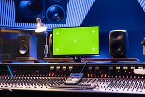 Empty control room with greenscreen on monitor and panel board, professional studio used for recording and editing tracks. Audio console helping with mixing and mastering music. photo