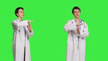 Woman physician doing timeout gesture against greenscreen backdrop, asking for a work break after multiple examinations. Doctor showing pause or stop symbol, feeling tired. Camera B. photo