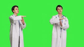 Woman physician doing timeout gesture against greenscreen backdrop, asking for a work break after multiple examinations. Doctor showing pause or stop symbol, feeling tired. Camera B. photo