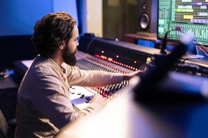 Music producer working on a new album in control room at studio, recording and processing sounds before editing in post production. Audio technician using daw software and mixing console. photo