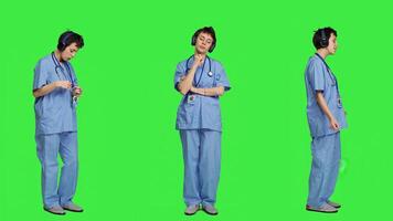 Cheerful health specialist listening to cool music on audio headset, dancing against greenscreen backdrop and having fun. Nurse enjoying songs an doing funny dance moves, leisure. Camera A. photo