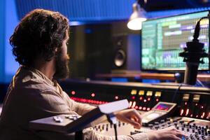 Sound designer editing music with digital audio software on pc, recording and processing sounds in control room. Young technician producing music with mixing console and faders. photo