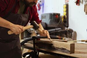 experto carpintero meticulosamente tallado intrincado diseños dentro madera utilizando cincel y martillo en montaje tienda. artesano en carpintería taller formación de madera piezas con herramientas foto