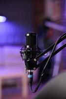 Close up shot of podcast microphone used to record conversations for internet livestreaming show. Streaming sound capturing and recording technology in empty home studio with neon lights photo