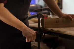 Woodworker using bench vise to hold lumber block, starting furniture assembling in workshop, close up shot. Craftsperson in joinery using vice tool to clamp piece of wood before carving it photo