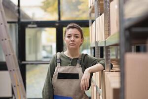 Warehouse manager standing in delivery service storage, preparing customers orders. Storehouse supervisor wearing industrial overall while working and coordinating goods supply chain photo