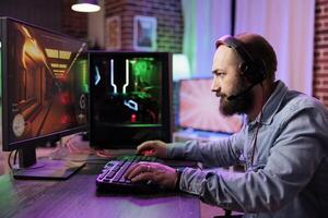 Pro gamer competing in intense online multiplayer game, streaming live from brick wall apartment. Focused man using gaming system and headphones for immersive experience photo