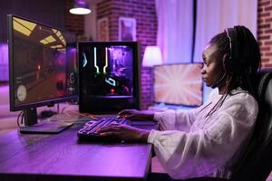 Woman in brick wall living room playing SF game on gaming PC at computer desk late at night. Tired gamer girl battling hostiles in online multiplayer futuristic shooter photo