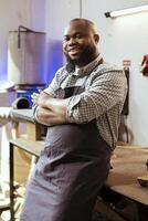 Portrait of smiling african american carpenter in woodworking shop proud of his work in furniture assembling business. Focus on happy BIPOC cabinetmaker in joinery having crafting occupation photo