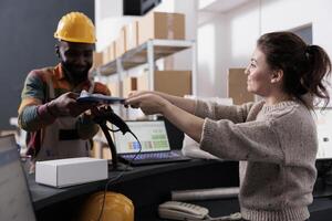 African american employee signing inventory report, discussing customers online orders before start preparing packages in warehouse. Supervisor standing at counter desk checking goods logistics photo