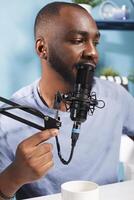 African american vlogger speaking in microphone on internet podcast channel. Young man blogger talking with subscribers in mic while broadcasting live and creating web content in studio photo