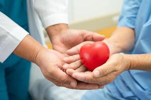 médico dar rojo corazón a asiático mayor mujer paciente en su mano en cama en hospital. foto