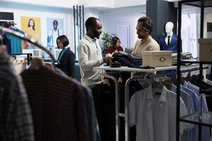 Smiling assistant holding hanger with stylish jacket, showcasing fashion trend to customer in clothing store. Boutique employee talking with client and helping to make apparel choice photo