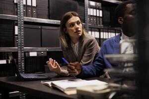 Diverse team reading accountancy report, working overhours at management research in storage room. Businesspeople analyzing administrative files, searching for bureaucracy record. photo