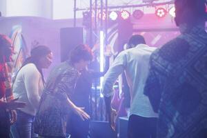 Cheerful clubbers laughing while improvising dance battle at discotheque in nightclub. Carefree man and woman friends showing moves on dancefloor while having fun at club party photo