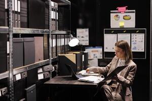 Manager analyzing administrative report, working late at night at bureaucracy record in arhive room. Corporate businesswoman reading accountancy documentation, trying to organizing files photo