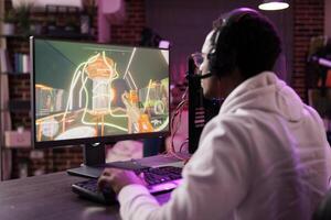 Man in brick wall living room playing games on gaming PC at computer desk, relaxing after work. Gamer facing enemies in online multiplayer shooter from rgb lights ornate home photo