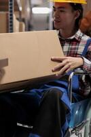 Asian warehouse order picker wheelchair user holding customer parcel. Young storehouse employee with disability preparing freight for shipment while working in inclusive workplace photo