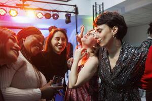 alegre sonriente mujer Bebiendo alcohol, abrazando y ir de fiesta juntos en Club nocturno. despreocupado diverso novias participación bebida anteojos, riendo y teniendo divertido en club foto