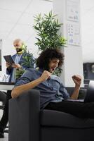 Excited start up company entrepreneur celebrating successful product launch. Happy young arab executive manager rejoicing effective marketing strategy while working on laptop in business office photo