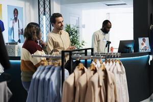 hombre asistente Ayudar mujer elegir ropa en compras centro comercial Moda boutique. ropa Tienda trabajador cliente preguntando trabajador para Consejo mientras seleccionando atuendo en sala de exposición foto