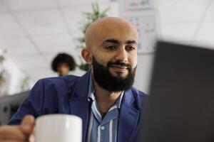 Smiling arab project manager checking customer email on laptop while working in business office. Company start up entrepreneur managing project on computer in coworking space photo