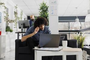 Project manager checking coworkers kpi on laptop in start up business office. Young arab entrepreneur thinking while solving complex problem on computer in corporate coworking space photo