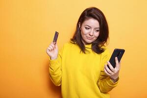 Portrait of caucasian lady gripping credit card to make purchase online with smartphone. Positive woman using internet banking and money to do shopping payment on mobile device. photo