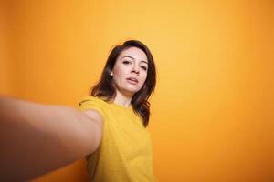 Cheerful gorgeous woman looking at camera taking picture using mobile device in studio with an isolated background. Smiling individual posing confidently for social media vlogging. photo