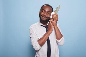 Young plant lover with eyes closed white pot with cactus to cheek showing love for houseplant. Smiling african american office worker with caring personality holding a potted plant. photo