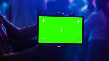 Adult using tablet with green screen at club, holding gadget with blank mockup template on dance floor. Young woman showing isolated display with chroma key and copyspace at nightclub. photo