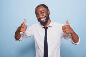 Portrait of african american man showing thumbs up sign in front of camera. Positive black individual giving like and approval, feeling happy and excited while advertising positivity. photo