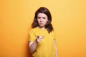Displeased woman with serious expression points her finger at the camera. Standing over isolated background, dissatisfied person who is upset and irritated makes frustrated and angry gesture. photo