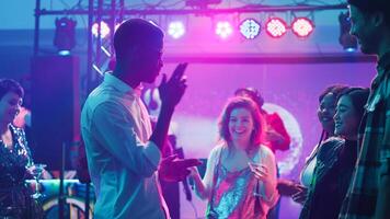 Casual man showing funky dance moves at club, moving on electronic music and having fun with friends. Group of modern people partying with DJ at audio station, packed dance floor. Tripod shot. photo