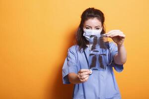 Portrait of doctor holding x-ray scan in front of the camera while wearing coronavirus mask. During covid19 epidemic, nurse practitioner examines the findings of chest radiography. photo