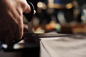 Extreme close up of suitmaker using scissors to cut refined textile material in atelier studio, showing expert meticulous craftmanship. Skilled tailor handcrafting bespoke garment piece photo