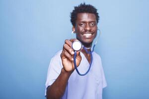 de cerca de africano americano cuidado de la salud especialista participación un estetoscopio hacia cámara. sonriente negro enfermero en uniforme avaro un médico instrumento para corazón o pulmón examen. foto