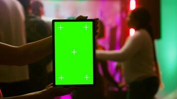 Girl showing greenscreen display at club holding blank chroma key display at party on dance floor. Modern person using isolated mockup screen with copy space template on device. Tripod shot. photo