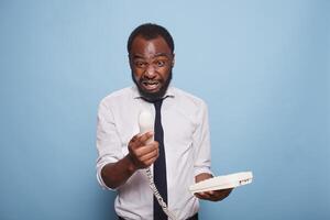 An enraged black businessman yells into the cord phone receiver, arguing with the person on the other end of the line. An anxious African American employee is on the phone with his manager. photo