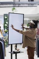 African american man interacting with digital screen offering shoes to customer in shopping center. Clothing store buyer touching white empty display mock up to check stiletto brand options photo