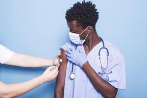 caucásico persona administrar vacuna inyección a africano americano enfermero en contra azul antecedentes. de cerca de un médico dando vacunación a negro hombre, asegurando cuidado de la salud y codicioso 19 prevención. foto