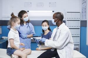 Doctor and nurse conducting a checkup, providing advice to a girl and her mother in a medical office. Healthcare professionals have a consultation with patients. Face masks worn for protection. photo