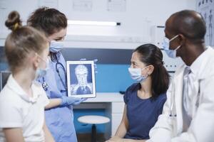 médico análisis un cerebro escanear mientras explicando el resultados, en un moderno clínica con estado de el Arte tecnología. enfermero participación un tableta mostrando un X rayo imagen de un cabeza de un paciente. foto