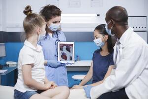 Black doctor shows cardiology image on digital tablet, pediatrician explains cardiovascular diagnosis to child and parent. Heart anatomy picture and heart disease problems presented by pediatrician. photo