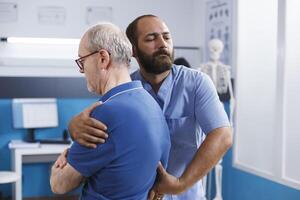 Elderly guy receiving rehabilitation from chiropractor for back pain and spinal injuries. Nurse practitioner helping retired patient heal from accident and providing chiropractic care for treatment. photo