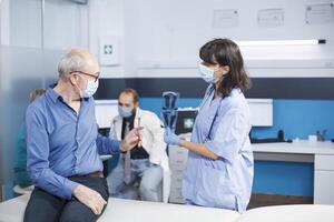 Nurse practitioner grasping ct scan results at medical consultation with elderly man during coronavirus pandemic. Healthcare specialist explains radiography diagnosis, finding lungs treatment. photo