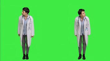 Woman physician looking around for patients to come at checkup exams, waiting for someone standing against greenscreen backdrop. General practitioner with white coat feeling impatient. Camera A. photo