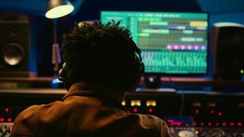 African american tracking engineer processing and mixing sounds in control room, operating audio console with moving faders and colored meters. Technician producer deals with technical gear. Camera B. photo