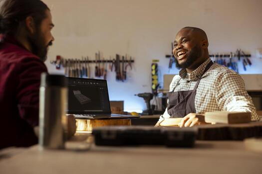 Happy carpenter looking over blueprints schematics on laptop in CAD software with cheerful apprentice. Smiling woodworker and joyful colleague having fun designing custom 3D furniture on notebook photo