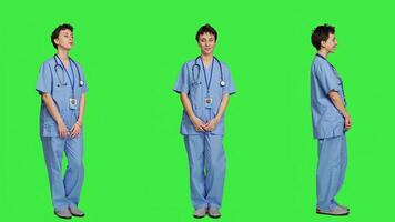 Portrait of medical assistant smiling and posing with confidence, standing against greenscreen backdrop. Nurse wears blue scrubs and stethoscope, feeling successful with health expertise. Camera A. photo